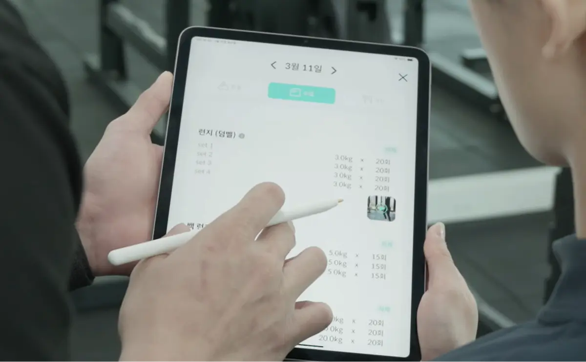 코치가 태블릿에 세트와 중량을 적는 모습